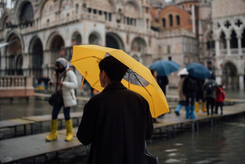 A person stands under an umbrella during heavy rain in Venice