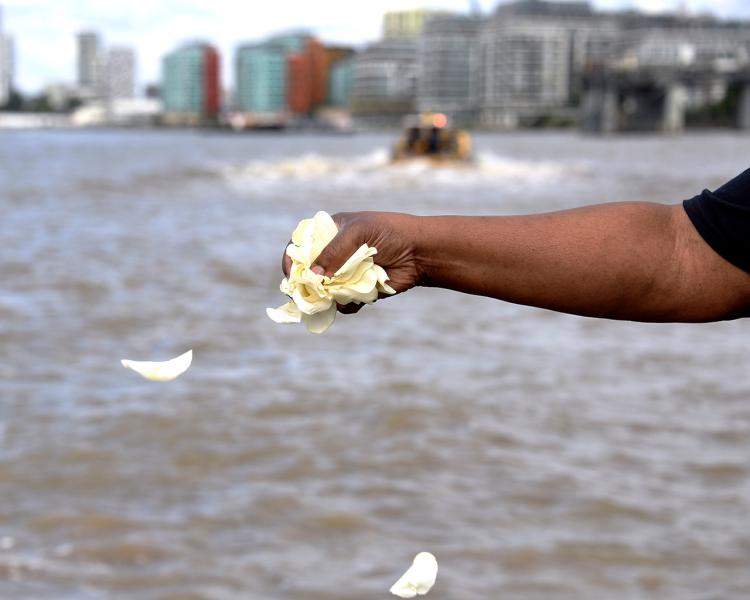 A close-up of a person's hand throwing petals into the river Thames