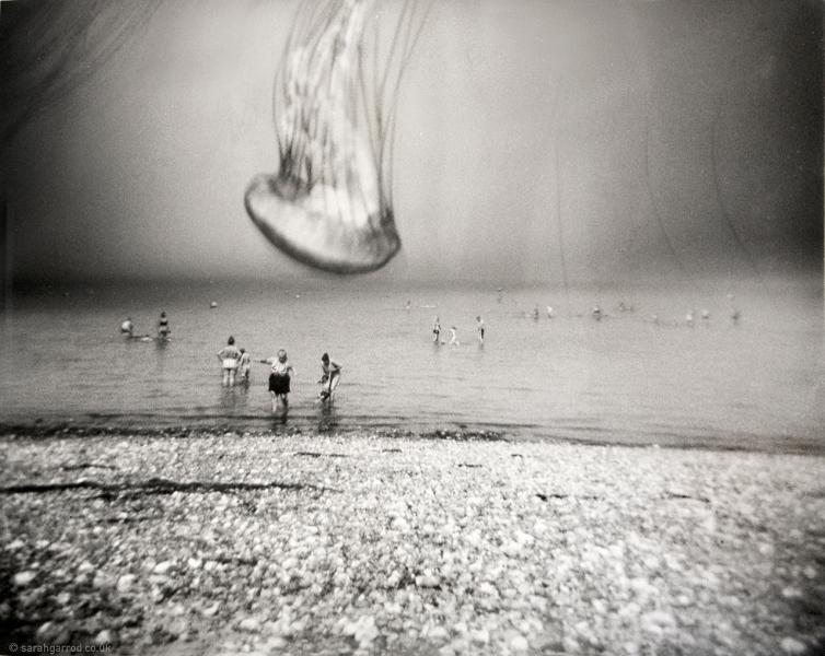 A black and white photograph of the seaside, with a jellyfish outline superimposed on top through photographic development