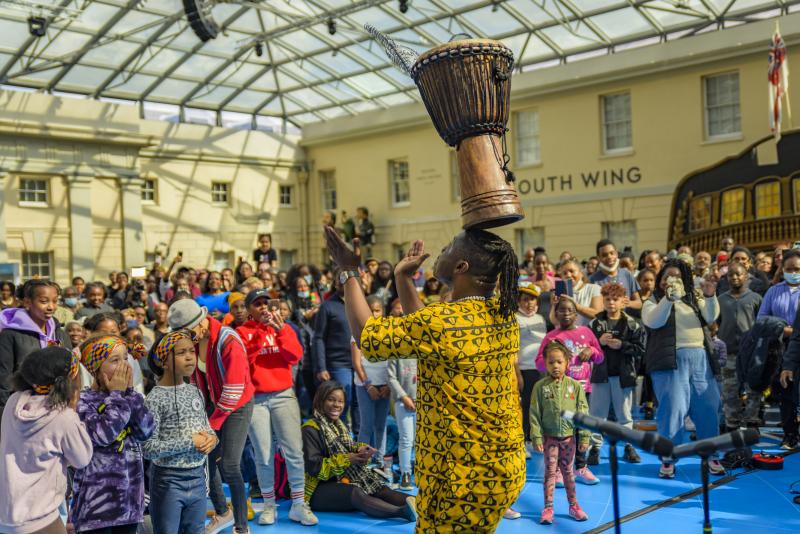 A man balances a drum on his head to applause from a big crowd