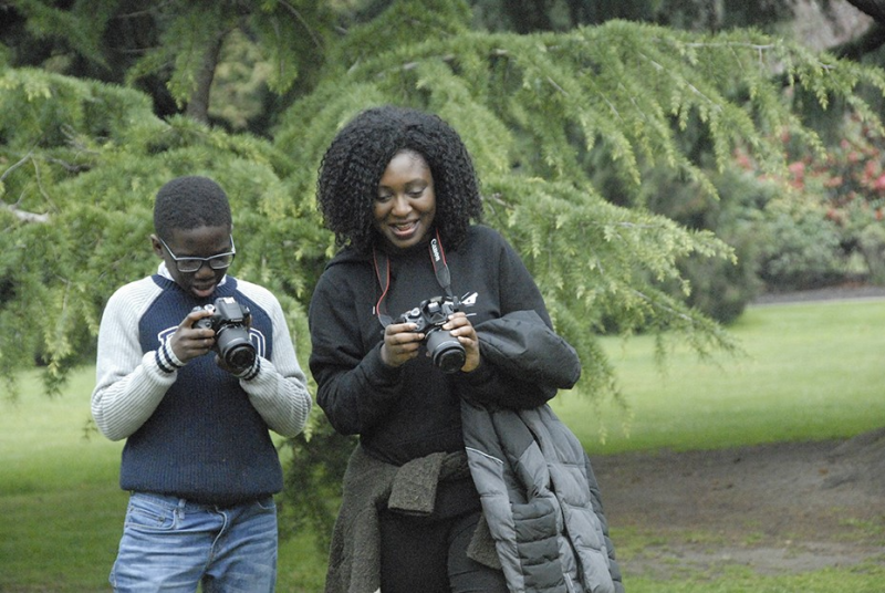 Two people look at their cameras in a park.