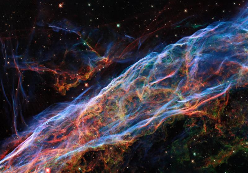 The Veil Nebula as seen by the Hubble Space Telescope. Filaments of blue, green, and red light cover the image, tracing different gases inside the curtain-like cloud.