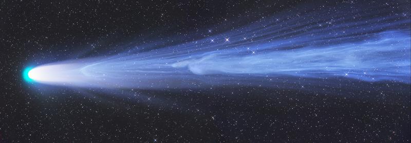Long, letterbox image with long blue and white comet in the middle. The tip of the comet faces to the left and is bright white, with an aqua crown. The tail is light blue, with the tail getting lighter and wavier as it goes along
