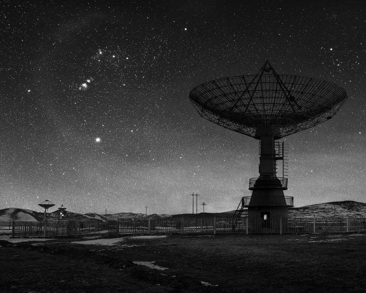 Black and white image of a radio telescope silhouetted against night sky