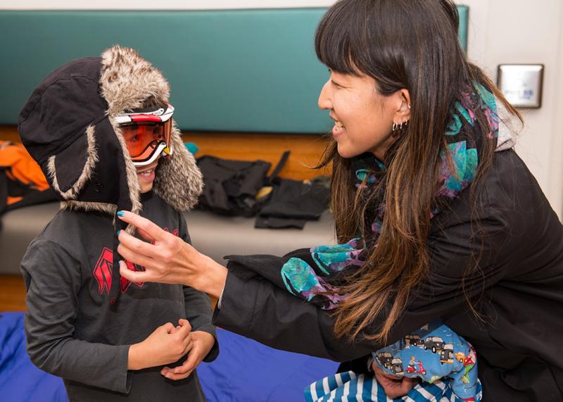 A child tries on a black puffer jacket and goggles