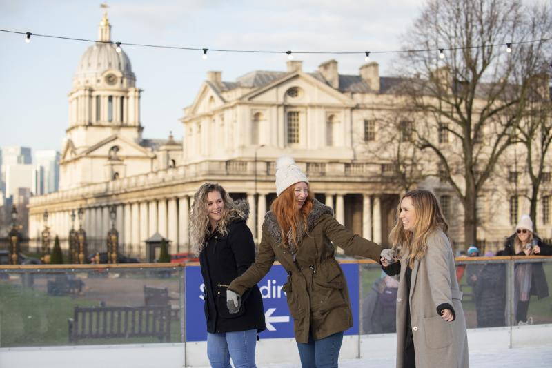 Three adult friends holding hands and having fun on the Queen's House Ice Rink, with Old Royal Naval College in background.jpg