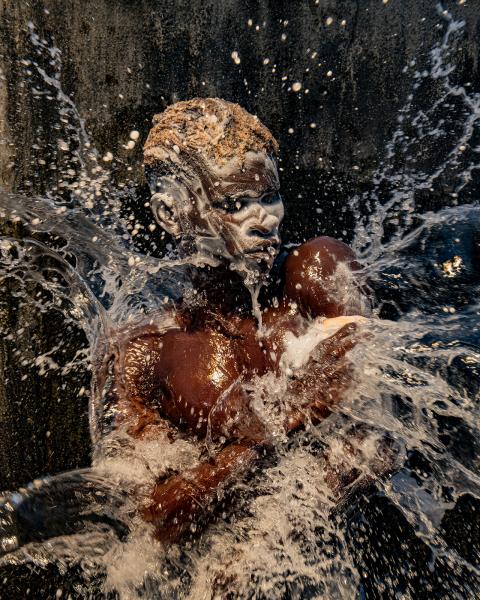 A photograph of a man washing. His face and hair is covered in soap suds, an water is being thrown over him