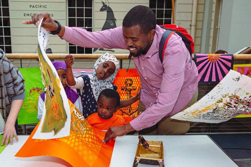 A family takes part in a print workshop during World Oceans Day at the National Maritime Museum. The father is peeling away a sheet of paper as two children look on