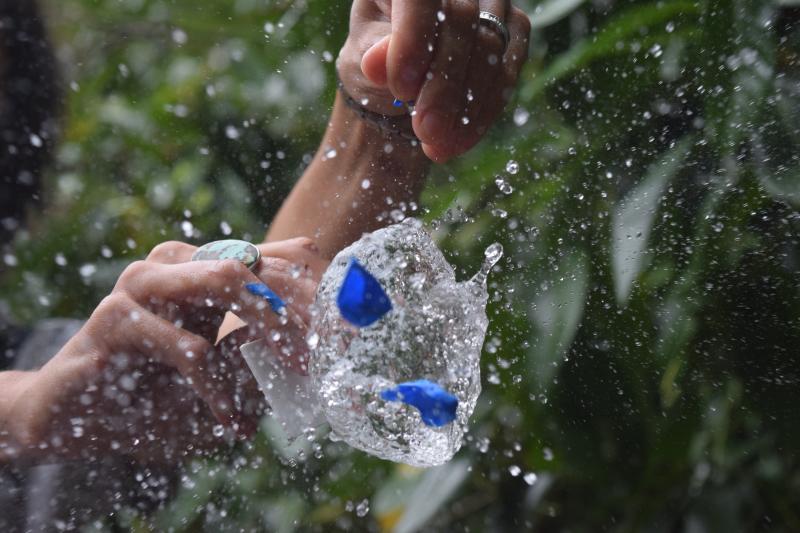 A photography of a water balloon popping and all the droplets coming out. Two hands are visible having let go when the balloon burst.