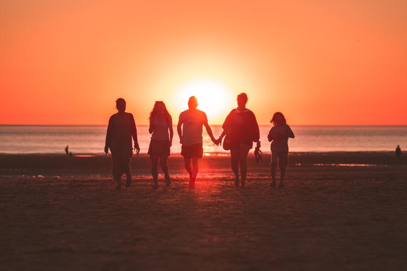 A family walks along a beach at sunset. The sun is setting behind them, framing them in silhouette
