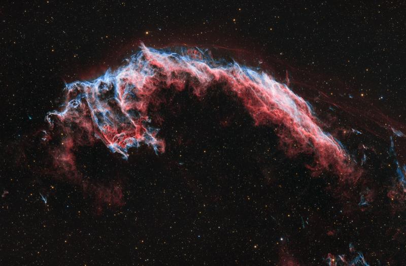 Deep space image showing the Veil Nebula, a glowing cloud of gas apparently floating in the darkness of space