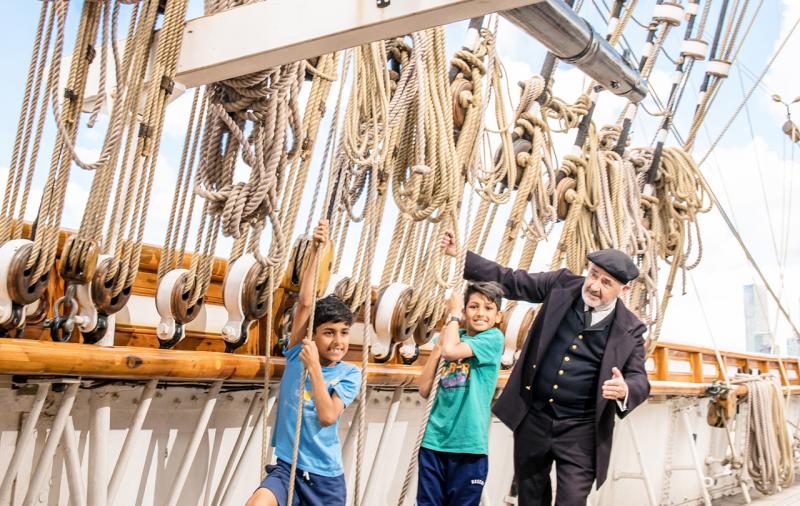 Two children pull on the ropes which are part of the tea clipper Cutty Sark's rigging, alongside captain Woodget