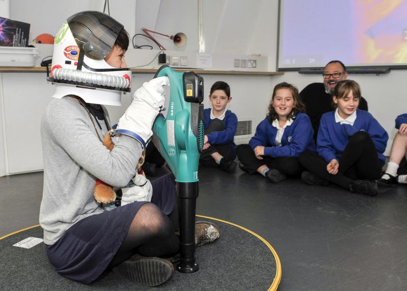 Children look on as a woman wearing an astronaut helmet gives a science demonstration
