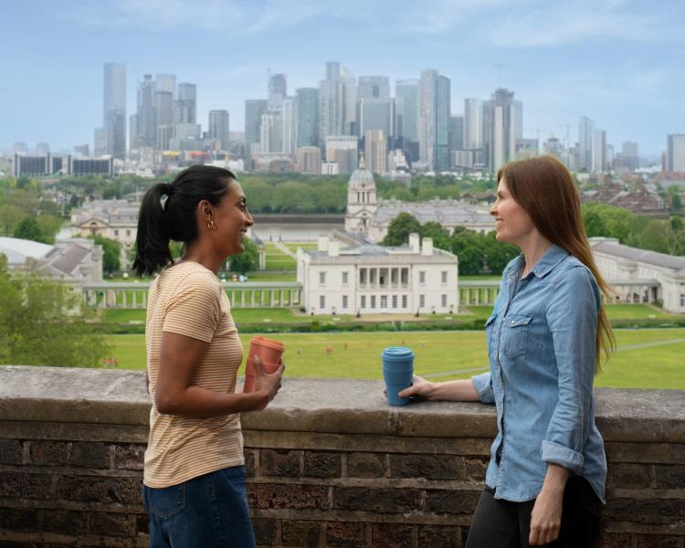 Two friends enjoy coffee with the view of Greenwich Park, the Queen's House and the skyline of Canary Wharf in the background