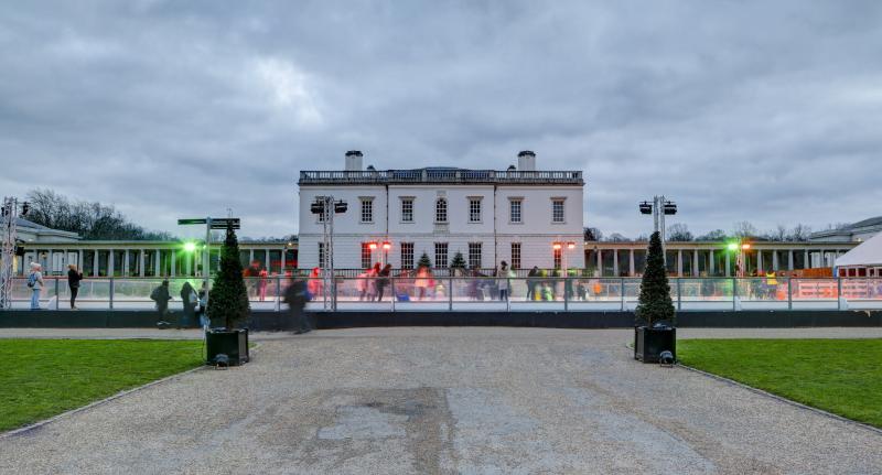 Image of the Queen's House Ice Rink at daytime, facing towards the Queen's House with red, green and yellow lights shining on the rink