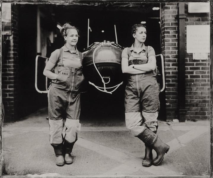 Black and white photograph of two women in overalls standing either side of a lifeboat