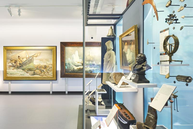 Glass display case with a number of Museum objects, next to an oil painting of an expedition to the Arctic