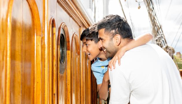 A father and son look through a porthole on the main deck of historic ship Cutty Sark